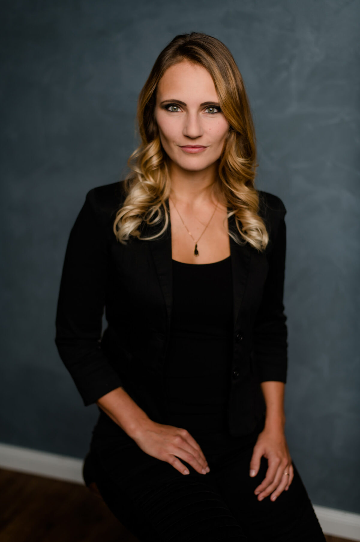 Christian Lorenz Fotograf Eine Frau mit blondem, gewelltem Haar, die einen schwarzen Blazer und ein schwarzes Oberteil trägt, sitzt vor einem dunklen, strukturierten Hintergrund und blickt selbstbewusst und mit neutralem Blick in die Kamera. Christian Lorenz Fotograf Eine Frau mit blondem, gewelltem Haar, die einen schwarzen Blazer und ein schwarzes Oberteil trägt, sitzt vor einem dunklen, strukturierten Hintergrund und blickt selbstbewusst und mit neutralem Blick in die Kamera.