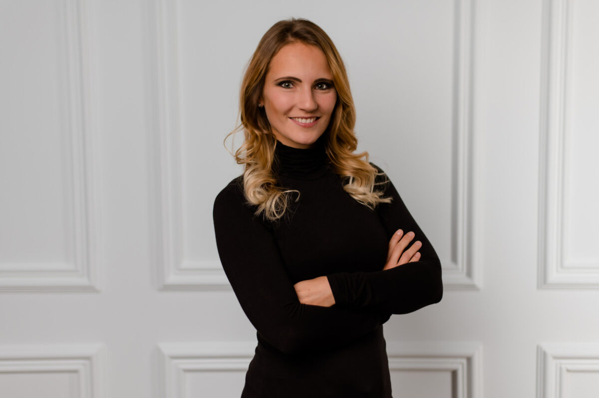Christian Lorenz Fotograf Eine Frau mit langen, gewellten blonden Haaren und einem schwarzen Rollkragenpullover steht mit verschränkten Armen und einem selbstbewussten Lächeln vor einer weiß getäfelten Wand. Christian Lorenz Fotograf Eine Frau mit langen, gewellten blonden Haaren und einem schwarzen Rollkragenpullover steht mit verschränkten Armen und einem selbstbewussten Lächeln vor einer weiß getäfelten Wand.