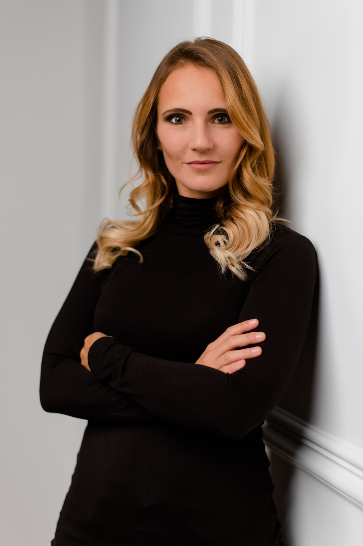 Christian Lorenz Fotograf Eine Frau mit gewelltem blondem Haar und schwarzem Rollkragenpulli steht mit verschränkten Armen vor einer weißen Wand und schaut selbstbewusst in die Kamera. Christian Lorenz Fotograf Eine Frau mit gewelltem blondem Haar und schwarzem Rollkragenpulli steht mit verschränkten Armen vor einer weißen Wand und schaut selbstbewusst in die Kamera.