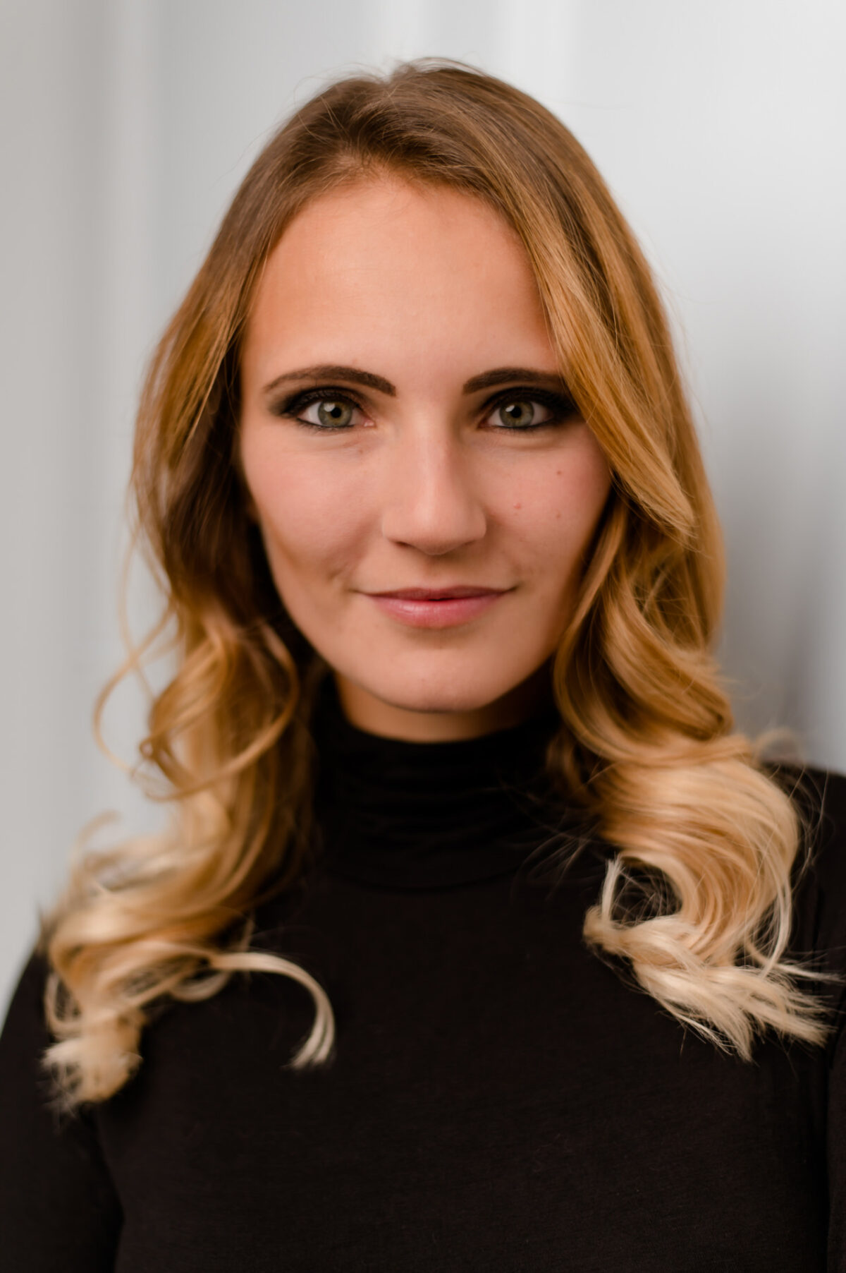 Christian Lorenz Fotograf Eine Frau mit gewelltem blondem Haar und schwarzem Rollkragenpullover lächelt sanft in die Kamera vor einem hellen, unscharfen Hintergrund. Christian Lorenz Fotograf Eine Frau mit gewelltem blondem Haar und schwarzem Rollkragenpullover lächelt sanft in die Kamera vor einem hellen, unscharfen Hintergrund.