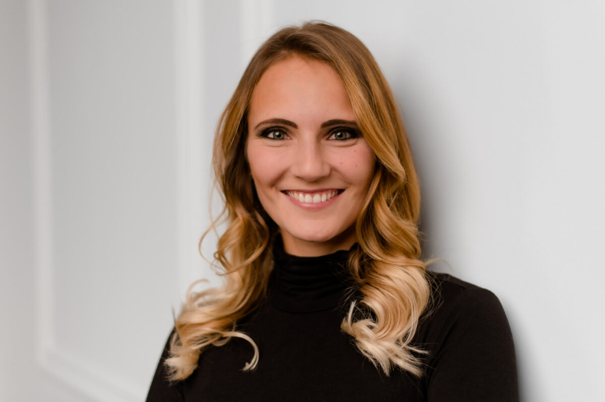 Christian Lorenz Fotograf Eine Frau mit gewelltem blondem Haar und schwarzem Rollkragenpullover lächelt in die Kamera, während sie an einer weißen Wand steht. Christian Lorenz Fotograf Eine Frau mit gewelltem blondem Haar und schwarzem Rollkragenpullover lächelt in die Kamera, während sie an einer weißen Wand steht.