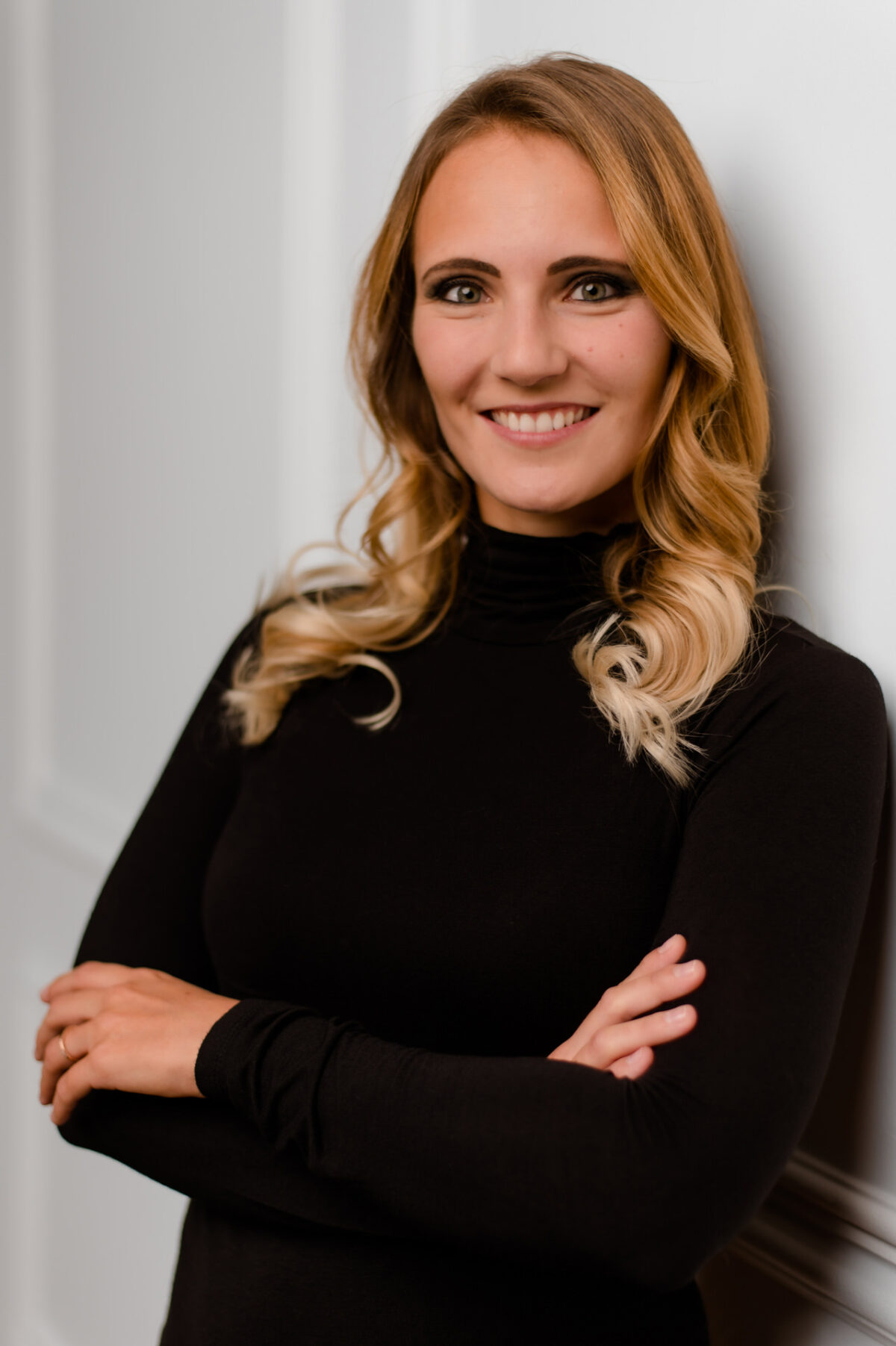 Christian Lorenz Fotograf Eine Frau mit langem blondem Haar und schwarzem Rollkragenpullover steht selbstbewusst lächelnd mit verschränkten Armen vor einer weißen Wand. Christian Lorenz Fotograf Eine Frau mit langem blondem Haar und schwarzem Rollkragenpullover steht selbstbewusst lächelnd mit verschränkten Armen vor einer weißen Wand.