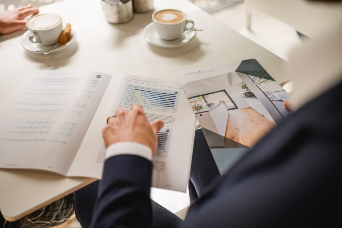 Christian Lorenz Fotograf Eine Person in Geschäftskleidung betrachtet gedruckte Tabellen und Diagramme an einem Tisch in einem Café, mit Kaffeetassen und Gebäck in der Nähe. Der Fokus liegt auf den Dokumenten und ihrer Hand, die auf die Daten zeigt. Christian Lorenz Fotograf Eine Person in Geschäftskleidung betrachtet gedruckte Tabellen und Diagramme an einem Tisch in einem Café, mit Kaffeetassen und Gebäck in der Nähe. Der Fokus liegt auf den Dokumenten und ihrer Hand, die auf die Daten zeigt.