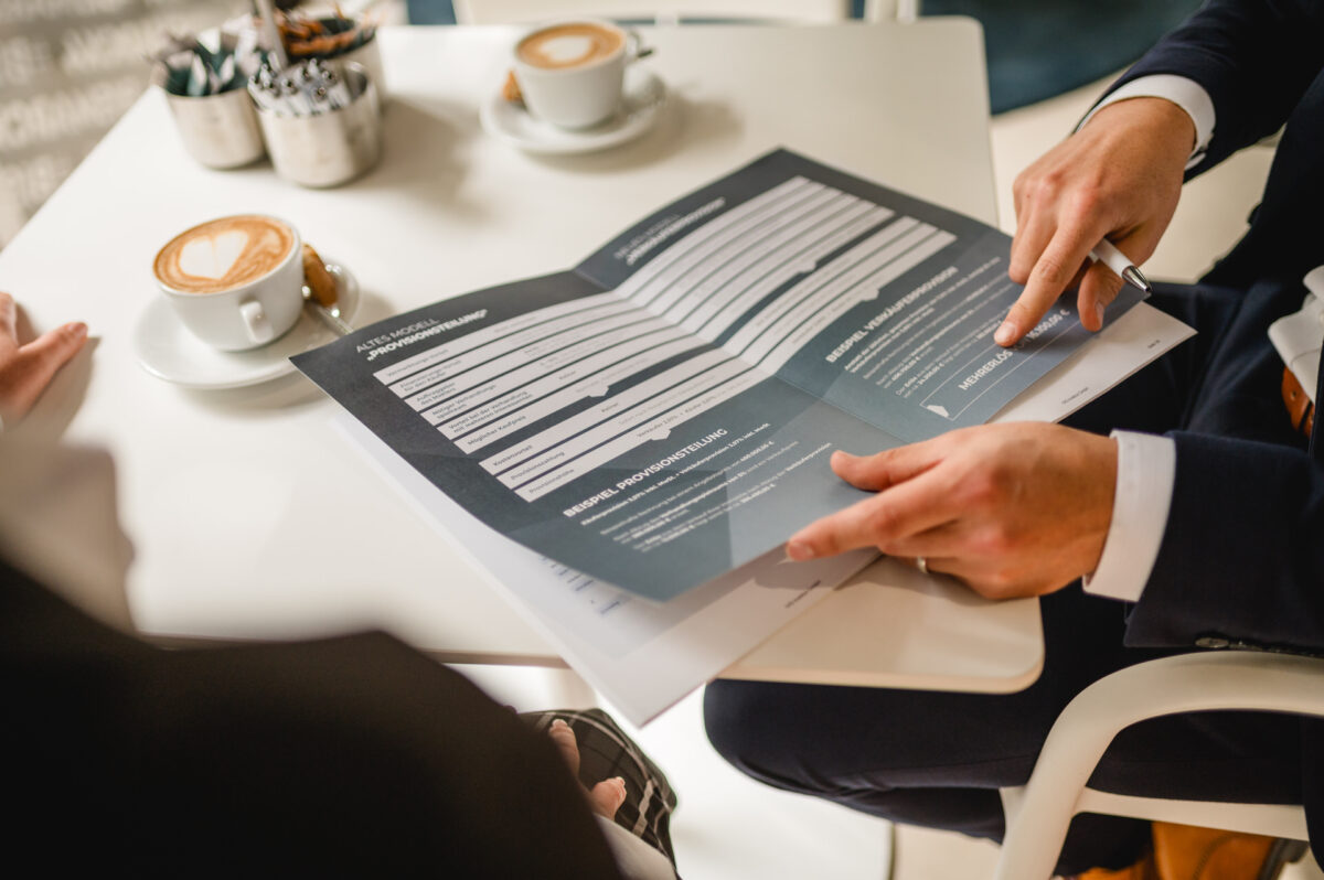 Christian Lorenz Fotograf Zwei Personen sitzen mit Kaffee an einem Tisch und gehen gemeinsam ein Dokument oder ein Formular durch. Eine Person zeigt auf einen Abschnitt des Dokuments, und auf dem Tisch stehen Kaffeetassen und kleine Behälter im Hintergrund. Christian Lorenz Fotograf Zwei Personen sitzen mit Kaffee an einem Tisch und gehen gemeinsam ein Dokument oder ein Formular durch. Eine Person zeigt auf einen Abschnitt des Dokuments, und auf dem Tisch stehen Kaffeetassen und kleine Behälter im Hintergrund.