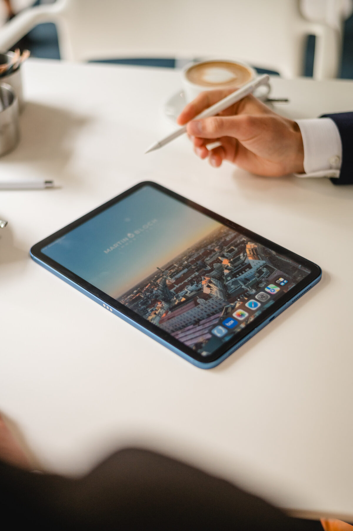 Christian Lorenz Fotograf Eine Person zeigt mit einem Stift auf ein Tablet, auf dem eine Stadtlandschaft auf einem weißen Tisch abgebildet ist, daneben stehen eine Tasse Kaffee, ein Stift und ein kleiner Behälter. Christian Lorenz Fotograf Eine Person zeigt mit einem Stift auf ein Tablet, auf dem eine Stadtlandschaft auf einem weißen Tisch abgebildet ist, daneben stehen eine Tasse Kaffee, ein Stift und ein kleiner Behälter.