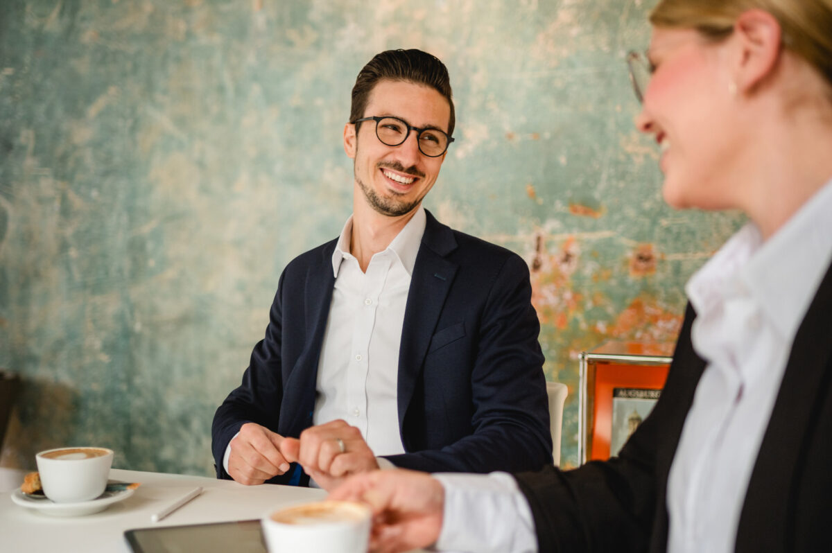 Christian Lorenz Fotograf Zwei Personen in Geschäftskleidung sitzen an einem Tisch mit Kaffeetassen, lächeln und unterhalten sich in einer entspannten Umgebung mit einer grünlichen, strukturierten Wand im Hintergrund. Christian Lorenz Fotograf Zwei Personen in Geschäftskleidung sitzen an einem Tisch mit Kaffeetassen, lächeln und unterhalten sich in einer entspannten Umgebung mit einer grünlichen, strukturierten Wand im Hintergrund.