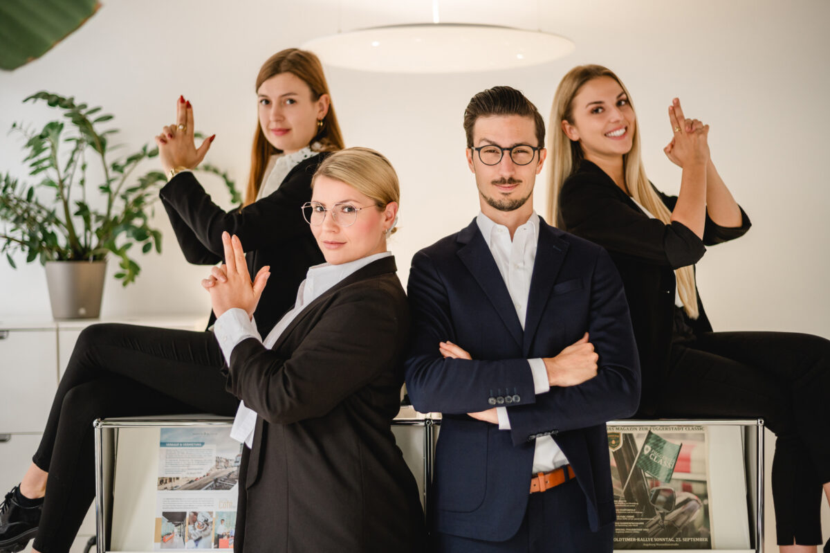 Christian Lorenz Fotograf Vier Geschäftsleute posieren selbstbewusst in einem Büro. Zwei Frauen in schwarzen Anzügen stehen vorne und machen mit den Händen eine Finger-Gun-Geste. Ein Mann in einem Anzug steht mit verschränkten Armen da. Zwei weitere Frauen im Hintergrund ahmen die gleiche Handbewegung nach. Christian Lorenz Fotograf Vier Geschäftsleute posieren selbstbewusst in einem Büro. Zwei Frauen in schwarzen Anzügen stehen vorne und machen mit den Händen eine Finger-Gun-Geste. Ein Mann in einem Anzug steht mit verschränkten Armen da. Zwei weitere Frauen im Hintergrund ahmen die gleiche Handbewegung nach.