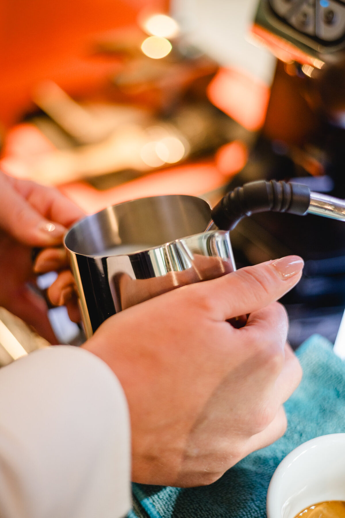 Christian Lorenz Fotograf Eine Person hält eine Metallkanne zum Aufschäumen von Milch unter einen Dampfstab und bereitet sich darauf vor, Milch für Kaffee zu kochen. Im Hintergrund sind die Espressomaschine und eine weiße Tasse zu sehen. Christian Lorenz Fotograf Eine Person hält eine Metallkanne zum Aufschäumen von Milch unter einen Dampfstab und bereitet sich darauf vor, Milch für Kaffee zu kochen. Im Hintergrund sind die Espressomaschine und eine weiße Tasse zu sehen.