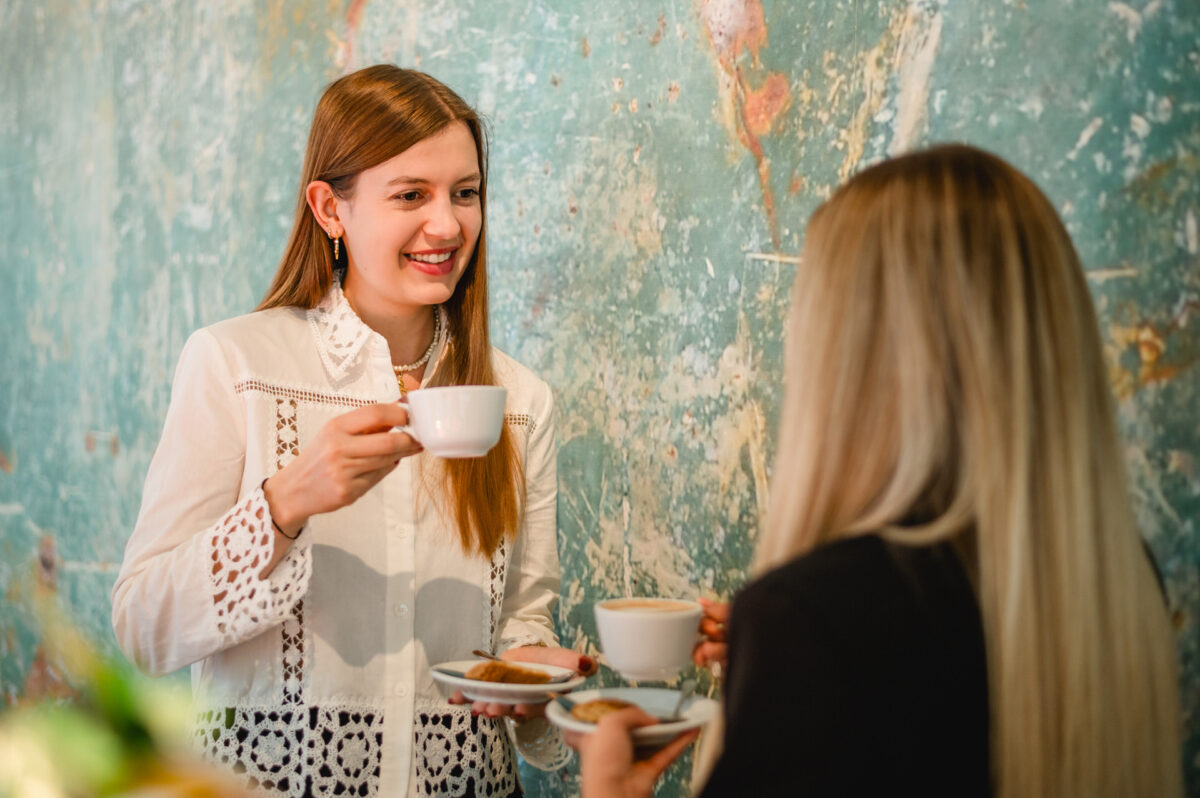 Christian Lorenz Fotograf Zwei Frauen stehen lächelnd mit Kaffee- oder Teetassen vor einer blau-grünen, strukturierten Wand. Eine Frau hält eine Untertasse mit Keksen in der Hand. Sie scheinen ein freundliches Gespräch zu führen. Christian Lorenz Fotograf Zwei Frauen stehen lächelnd mit Kaffee- oder Teetassen vor einer blau-grünen, strukturierten Wand. Eine Frau hält eine Untertasse mit Keksen in der Hand. Sie scheinen ein freundliches Gespräch zu führen.