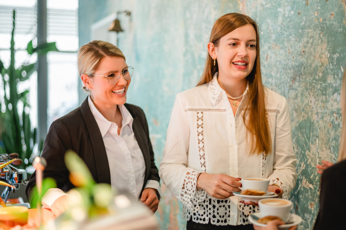 Christian Lorenz Fotograf Zwei Frauen stehen in einem Haus, lächeln und halten Tassen und Untertassen in der Hand. Sie scheinen sich in einem zwanglosen, geselligen Rahmen mit einer grün strukturierten Wand im Hintergrund zu unterhalten. Christian Lorenz Fotograf Zwei Frauen stehen in einem Haus, lächeln und halten Tassen und Untertassen in der Hand. Sie scheinen sich in einem zwanglosen, geselligen Rahmen mit einer grün strukturierten Wand im Hintergrund zu unterhalten.